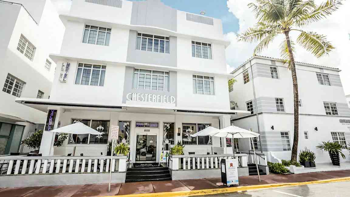 Et hvitt hotell i moderne arkitektur med store vinduer og en veranda med parasoller. (AI-generert tekst)