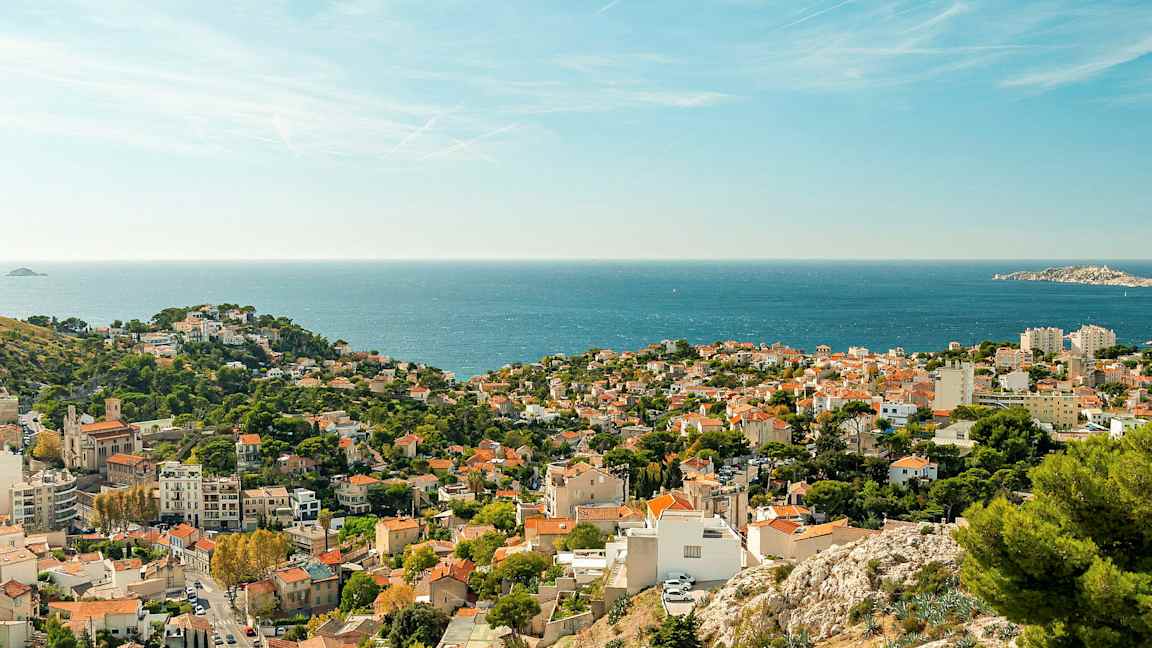 Utsikt over en kystby med røde tak og grøntområder, samt havet i bakgrunnen. (AI-generert tekst)