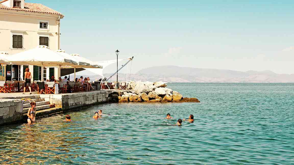 Folk svømmer i sjøen nær en kafé ved stranden. (AI-generert tekst)