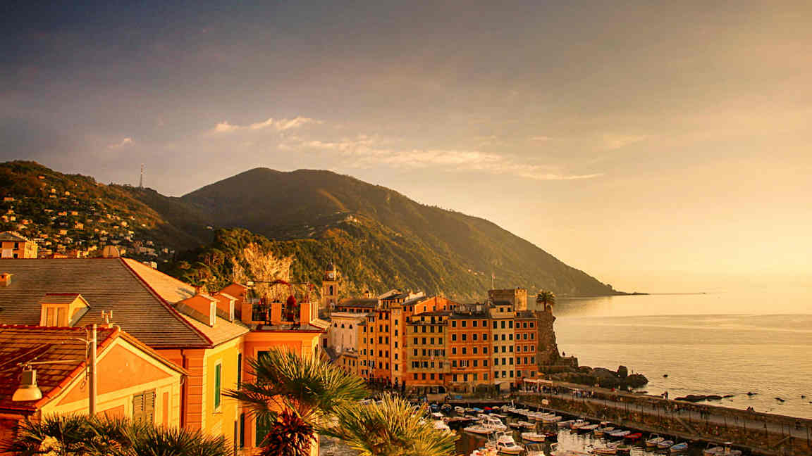 Bilde av en kystby ved havet med små båter i havnen og fjell i bakgrunnen. (AI-generert tekst)