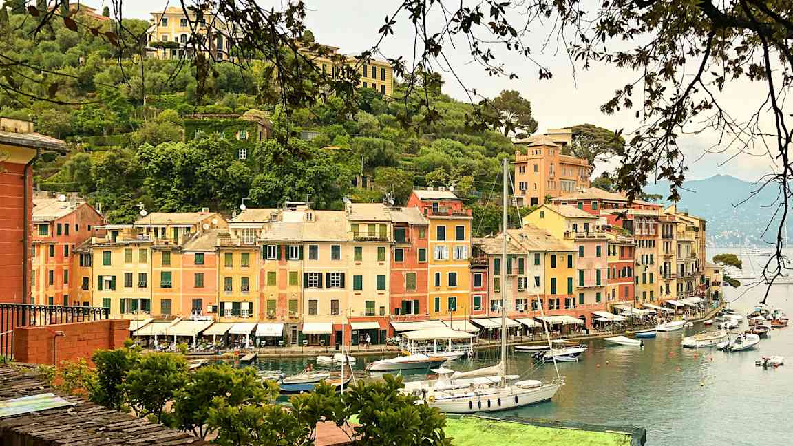 En havn med fargerike bygninger og seilbåter ved vannet. (AI-generert tekst)