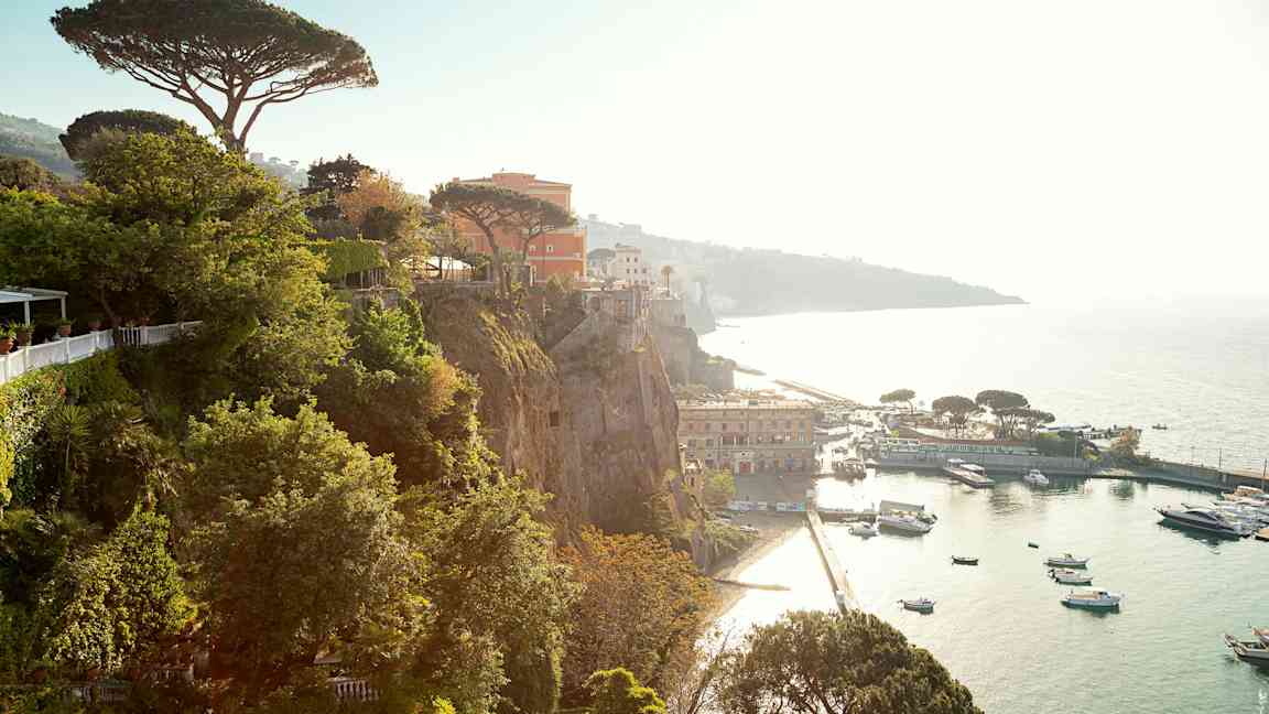 Utsikt fra klippe over havn med båter og bygninger. (AI-generert tekst)