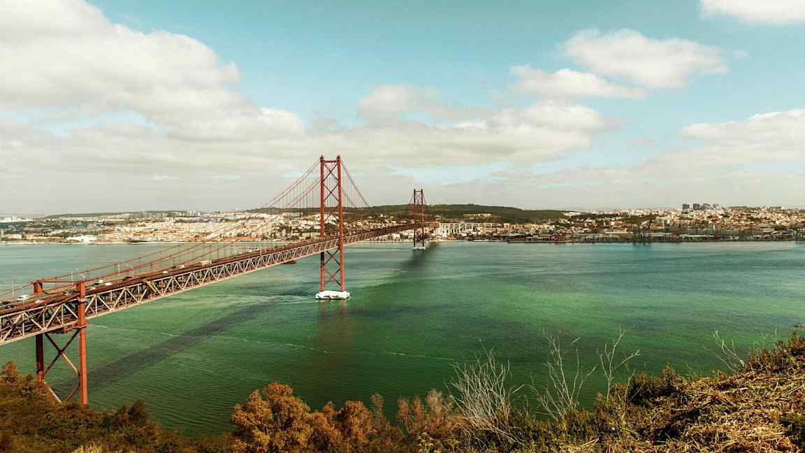 Bildet viser en rød bro over vann med en by i bakgrunnen. (AI-generert tekst)