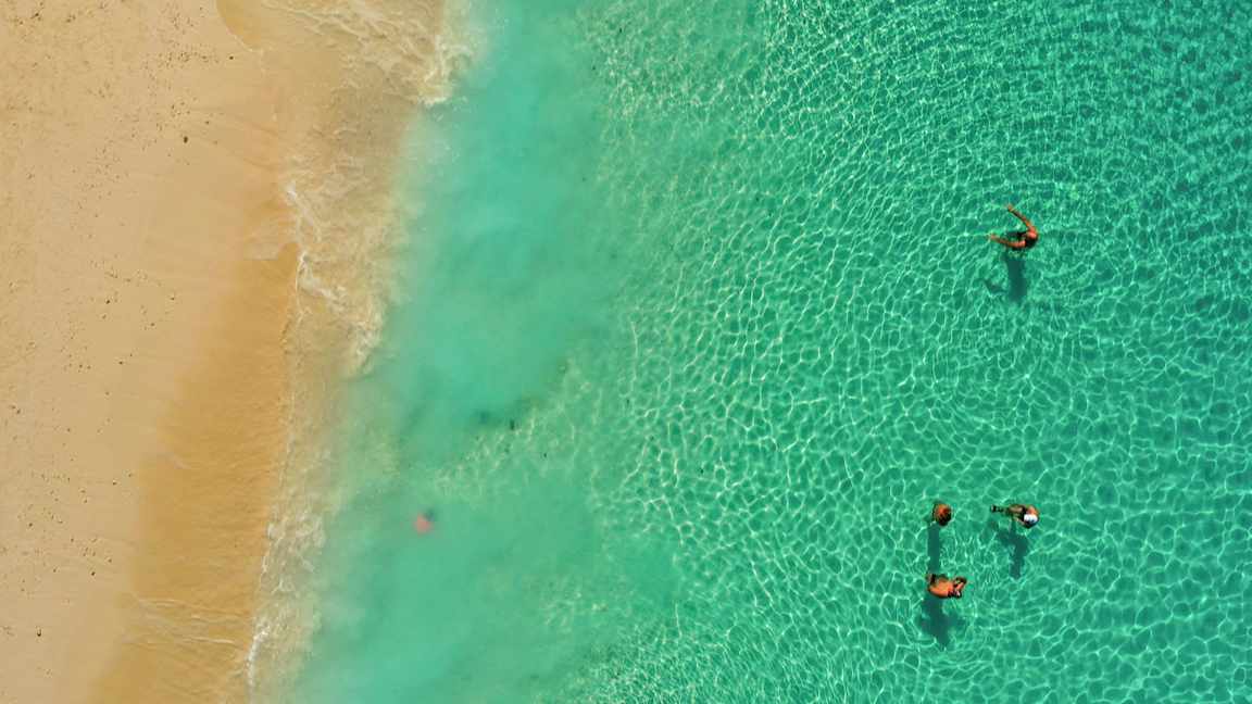 Dronefoto av personer som svømmer i sjøen nær en sandstrand. (AI-generert tekst)