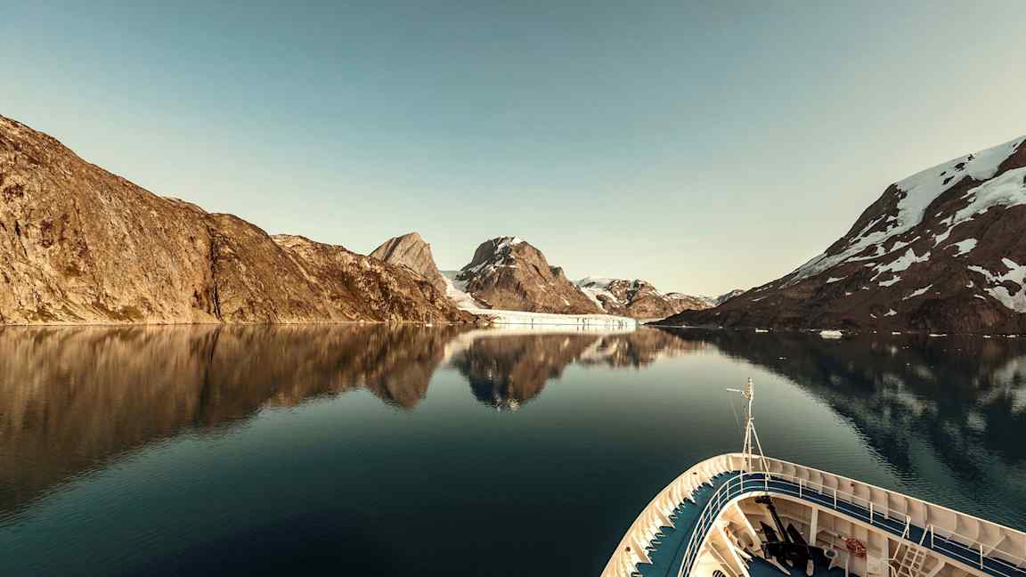 Et skip i en rolig fjord omgitt av fjell med snø. (AI-generert tekst)
