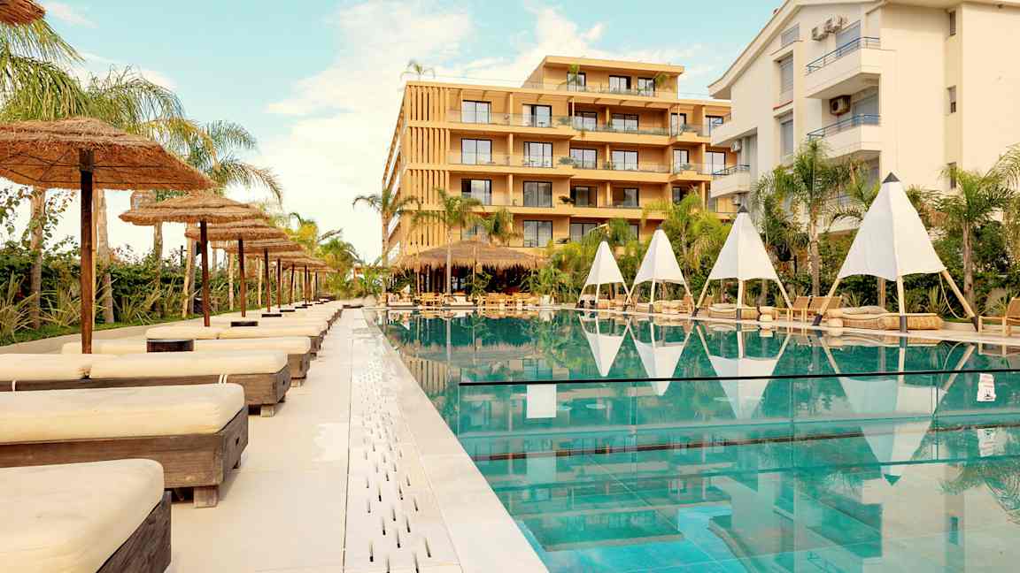 Utendørs svømmebasseng med solsenger og parasoller ved et hotell. (AI-generert tekst)