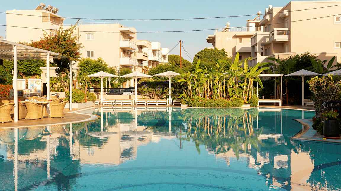 Bassengområde med parasoller, solsenger og bygninger i bakgrunnen. (AI-generert tekst)