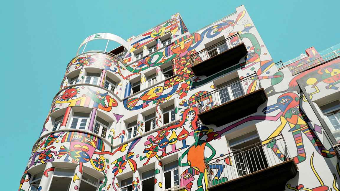 Bygning med fargerike abstrakte malerier på fasaden mot en klar blå himmel. (AI-generert tekst)