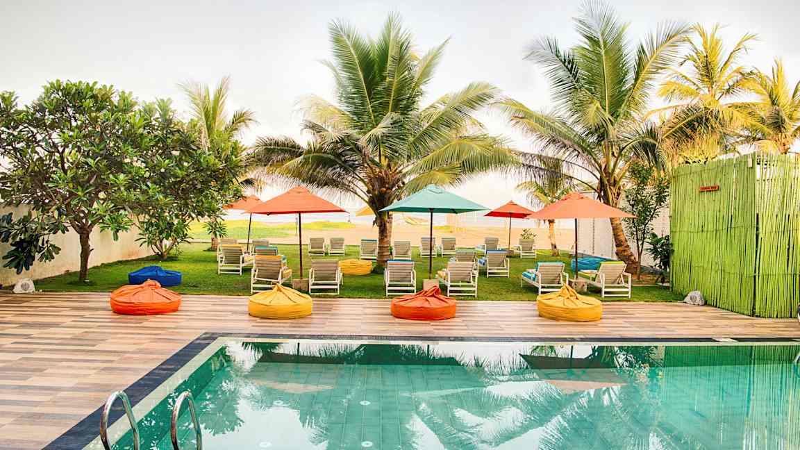 Et basseng med solsenger og fargerike parasoller i en hage omgitt av palmer. (AI-generert tekst)