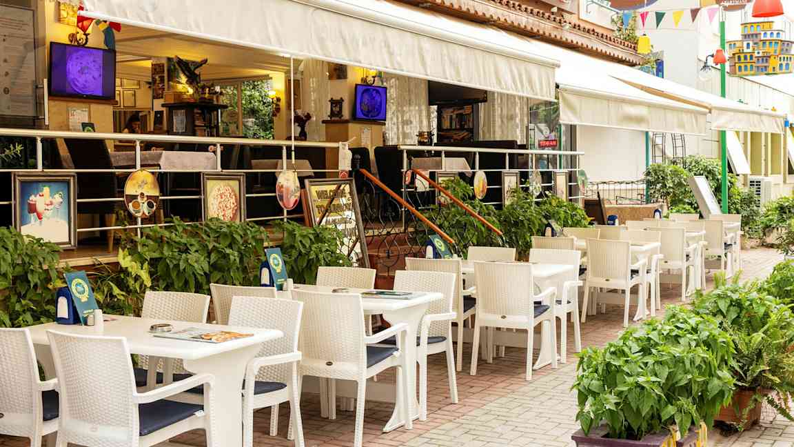 Restaurant med uteservering med hvite bord og stoler ved et hotell. (AI-generert tekst)