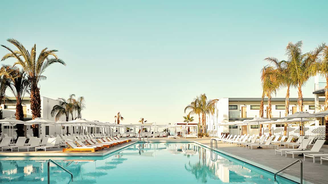 Et svømmebasseng omgitt av solsenger og palmer ved et hotell. (AI-generert tekst)