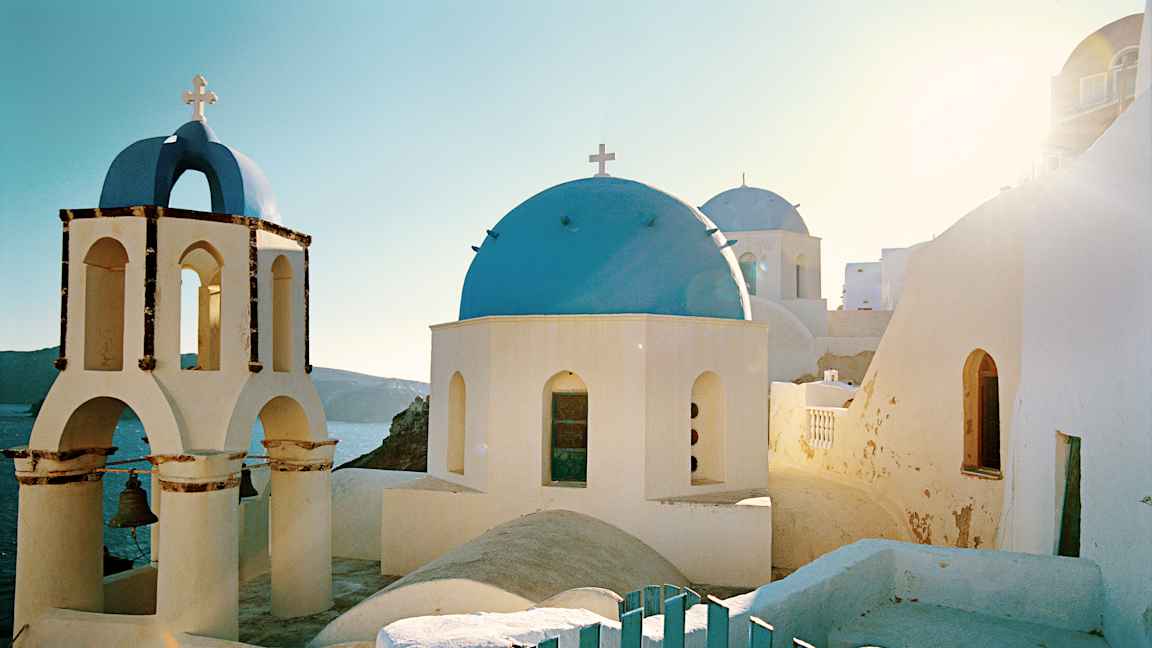 En hvit bygning med blå kuppel og klokketårn i solfylt landskap. (AI-generert tekst)