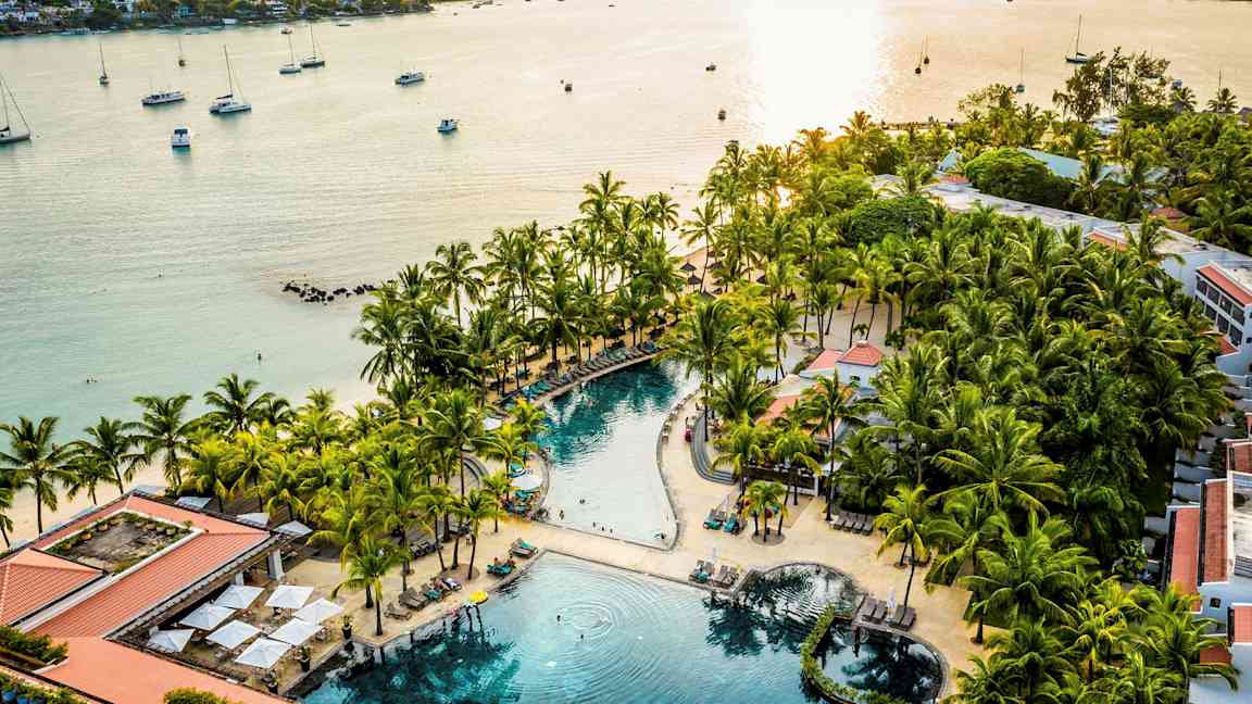 En strandresort med et basseng omgitt av palmer og solsenger nær sjøen. (AI-generert tekst)