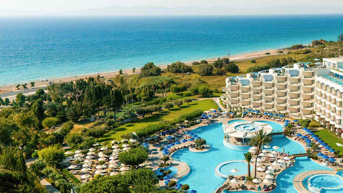 Utsikt over en resort med bassengområder, solsenger, grøntområder og havet i bakgrunnen. (AI-generert tekst)