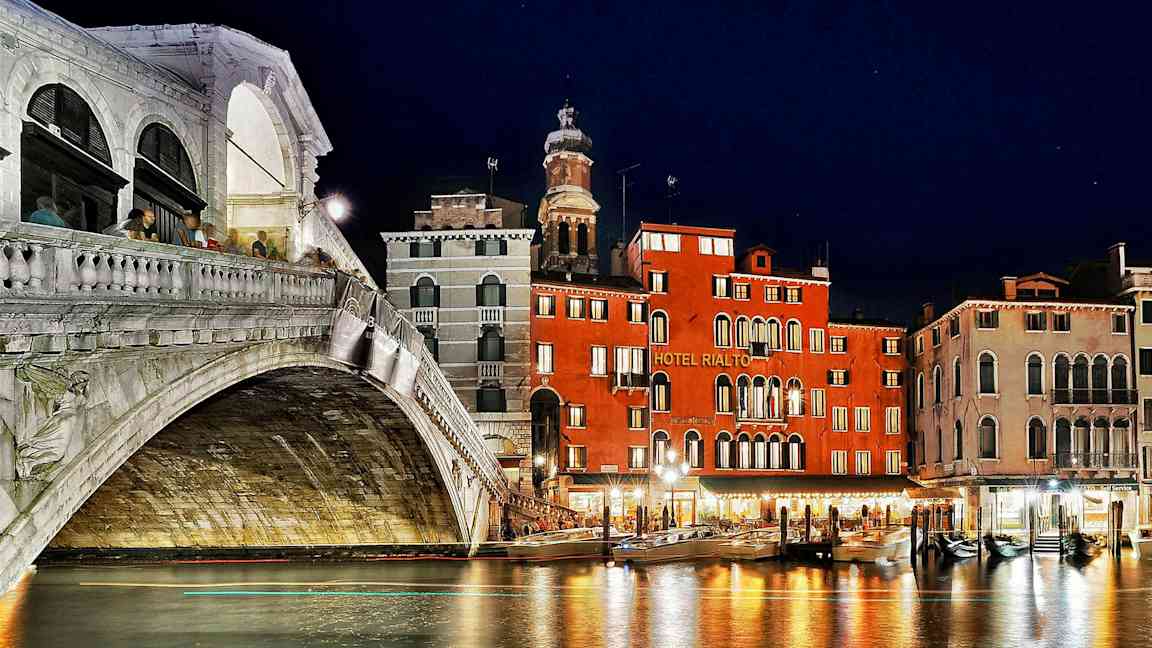 En nattutsikt av Rialto-broen og nærliggende bygninger ved Grand Canal i Venezia. (AI-generert tekst)