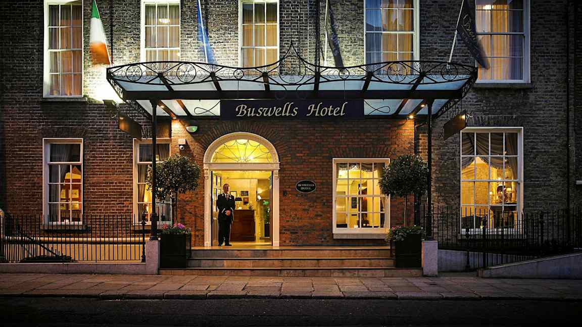 Inngangen til Buswells Hotel med en murfasade, flagg og innbydende belysning. (AI-generert tekst)