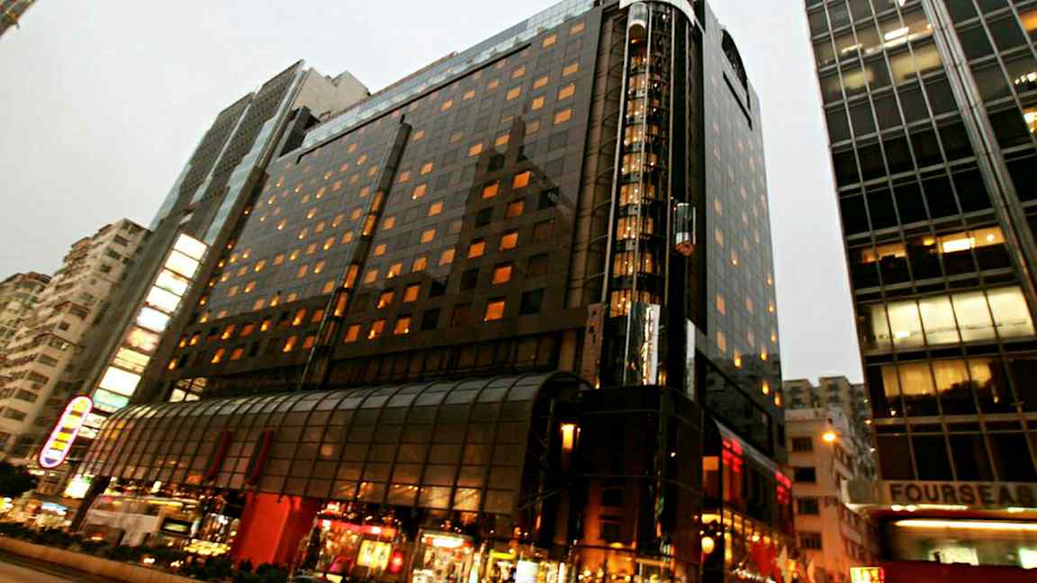 En opplyst bygning i flere etasjer i et bymiljø med glassfasade og gateliv i forgrunnen. (AI-generert tekst)