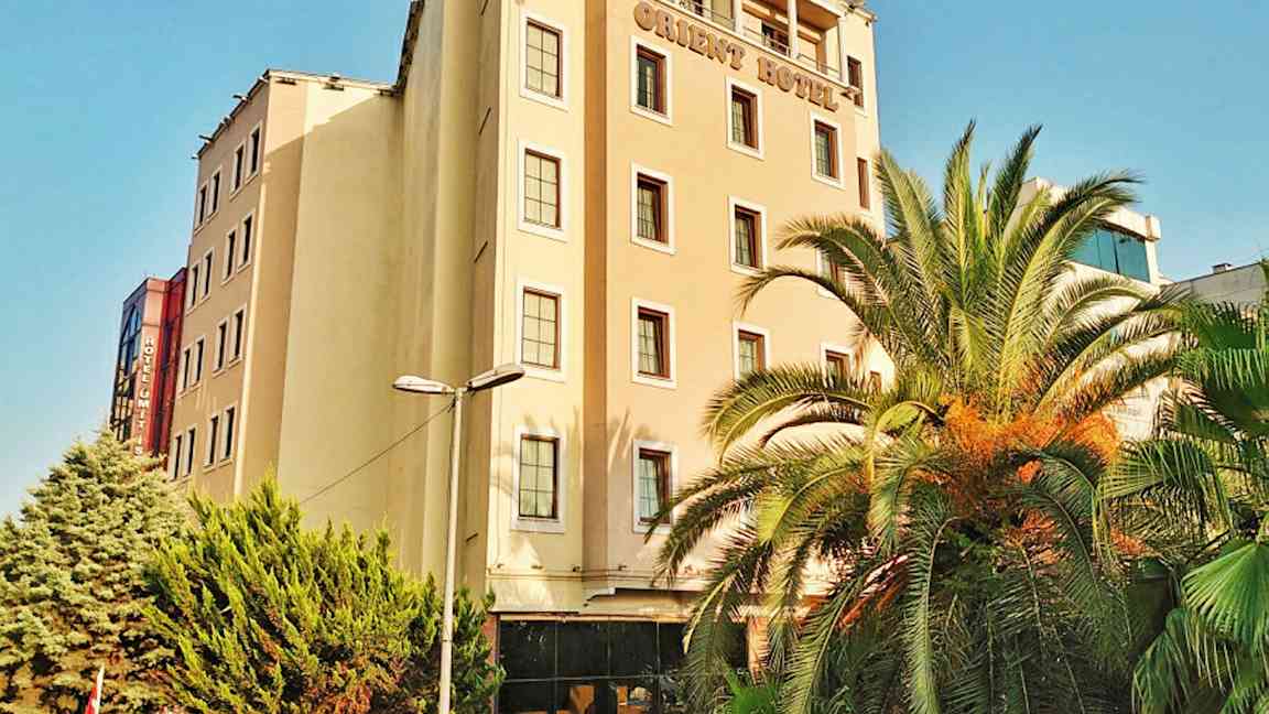 En hotellbygning med flere etasjer. Det er palmer og grønne trær foran bygningen. (AI-generert tekst)