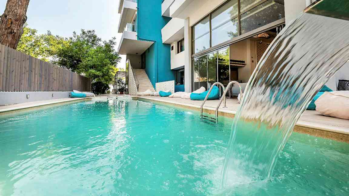 Utendørs svømmebasseng med fossefall ved en moderne bygning. (AI-generert tekst)