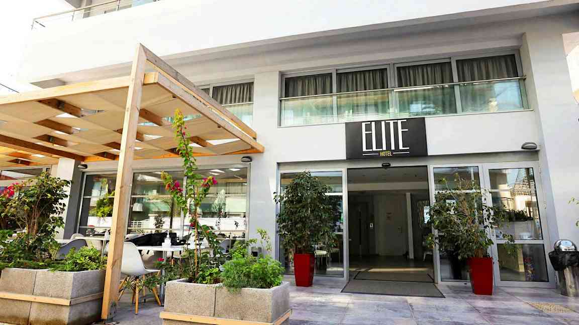 Hotellinngang med skilt som viser 'Elite Hotel', omgitt av planter og blomster. (AI-generert tekst)