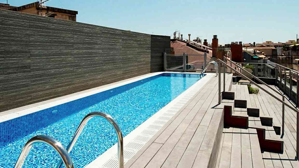 En takterrasse med et langt basseng omgitt av terrassebord og noen sitteplasser på siden. (AI-generert tekst)