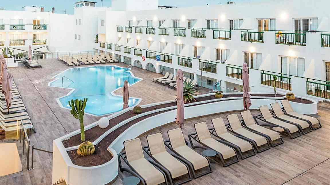 Et hotellbasseng med solsenger og en hvit bygning rundt. (AI-generert tekst)