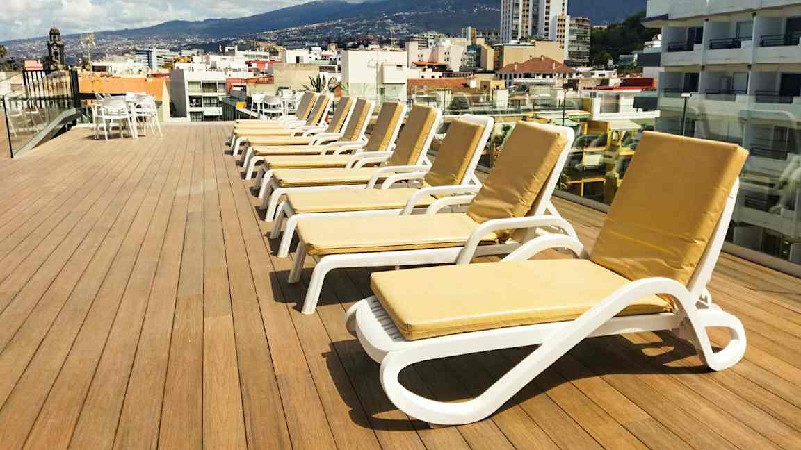 En takterrasse med solsenger og utsikt over en by og omkringliggende fjell. (AI-generert tekst)