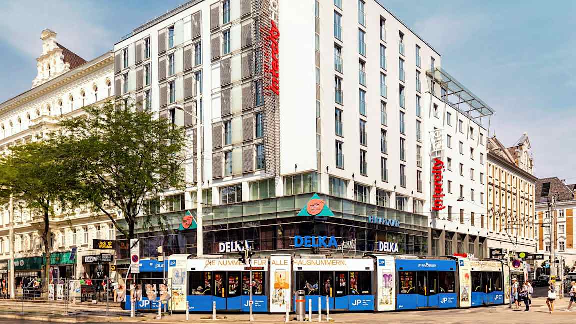 En flerfarget trikk foran et moderne hotell i bymiljø. (AI-generert tekst)