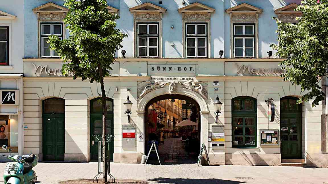 En bygning med vinduer, buede innganger og blomsterkasser på vinduskarmene. (AI-generert tekst)