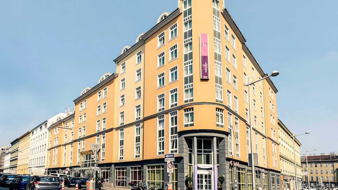 En lysgul bygning med mange vinduer, et skilt og buet hjørnefasade. (AI-generert tekst)