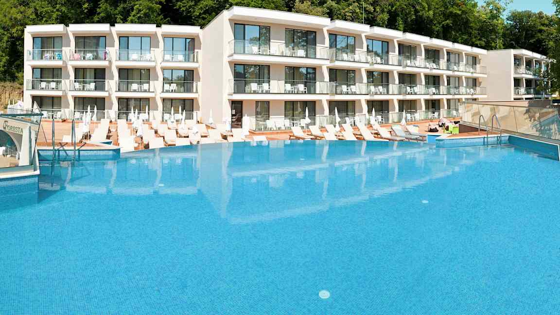 Hotellkompleks med et stort basseng foran og solsenger rundt. (AI-generert tekst)