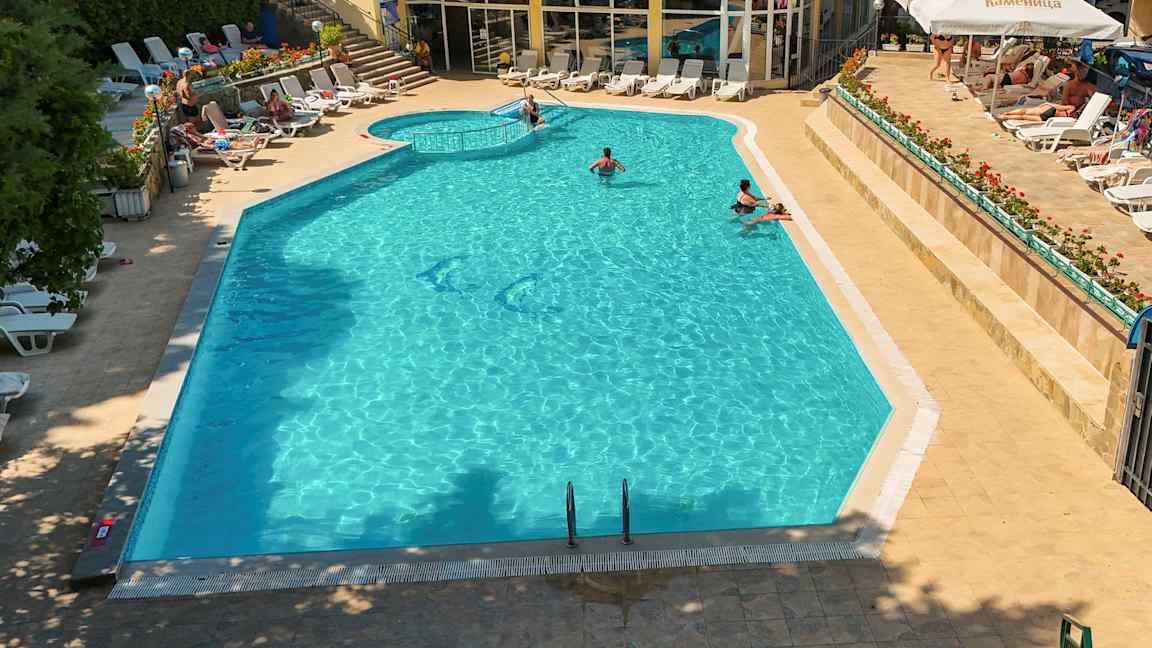 Et sommerhotellbassengområde med solsenger og folk som bader i bassenget. (AI-generert tekst)