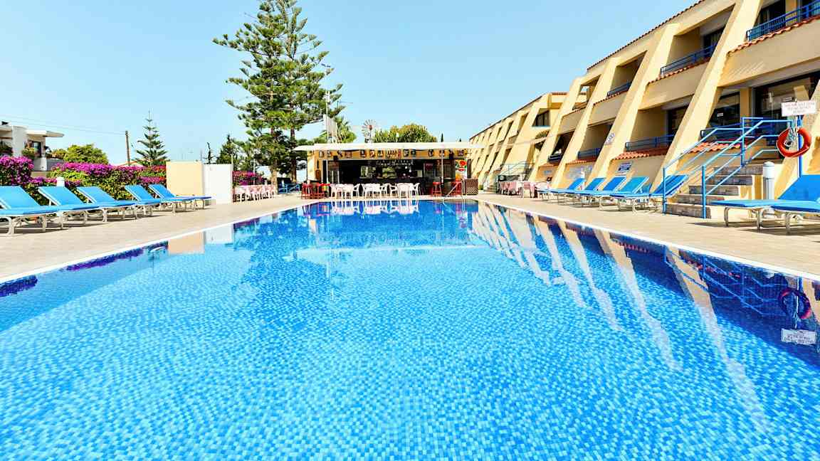 Et hotellområde med et basseng i forgrunnen, solsenger på begge sider og en bar i bakgrunnen. (AI-generert tekst)