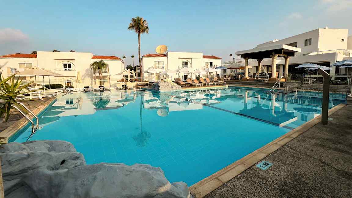 Et utendørs basseng foran hvite bygninger med røde tak. (AI-generert tekst)