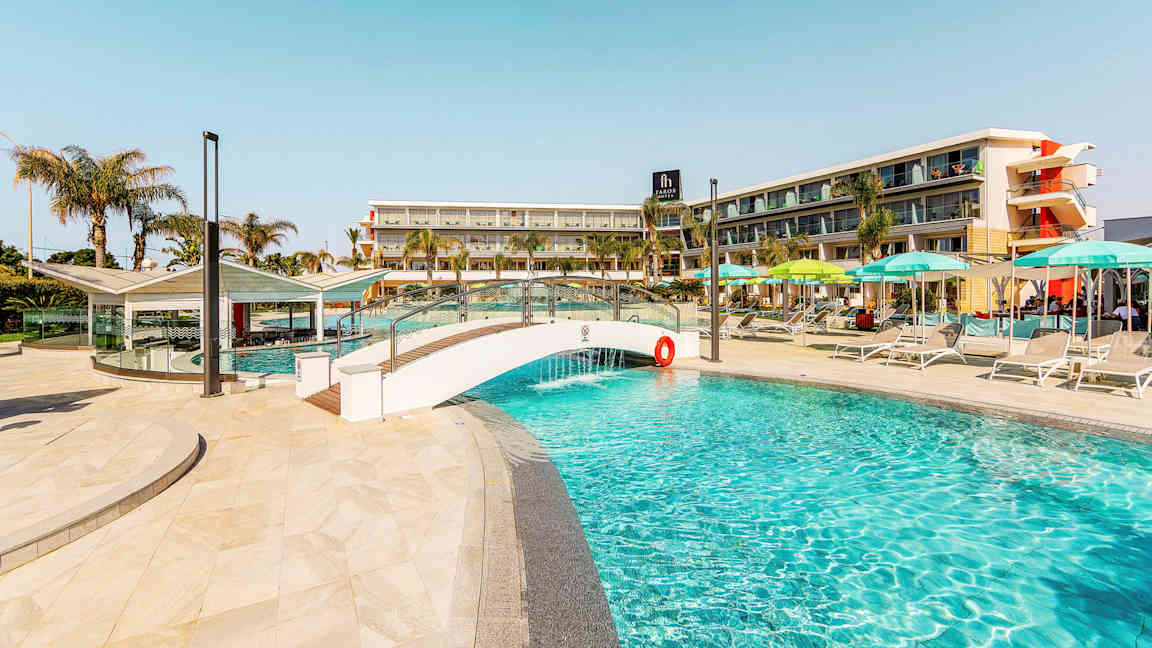 Bilde av et basseng, med en liten bro og hotellbygning i bakgrunnen. (AI-generert tekst)