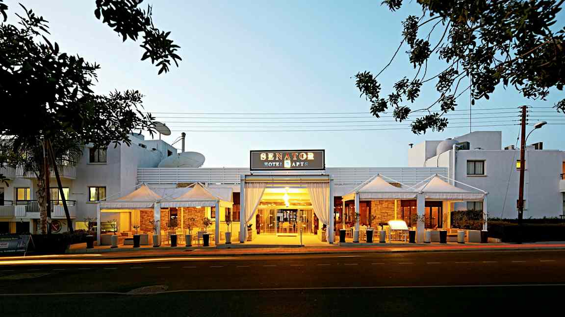 Inngangen til Senator Hotel Apartments med kveldsbelysning. (AI-generert tekst)