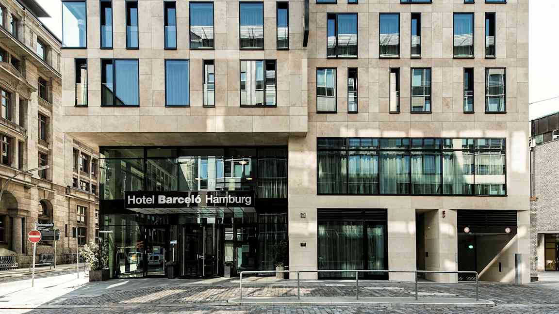 Et bygg med en moderne fasade og en inngang hvor det står "Hotel Barceló Hamburg". (AI-generert tekst)