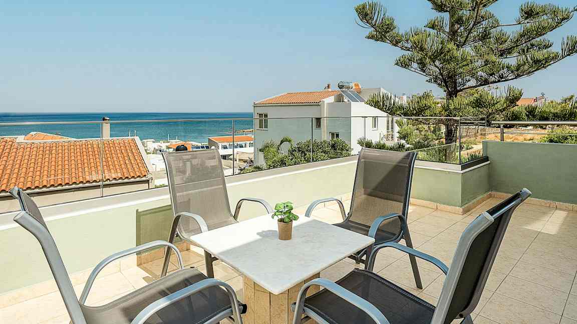 En terrasse med stoler og bord samt utsikt over havet og omkringliggende hus. (AI-generert tekst)