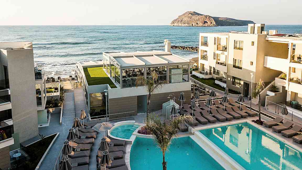 Hotellbygninger med basseng og solsenger nær sjøen. (AI-generert tekst)