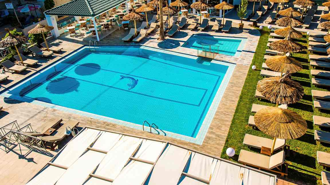 Et basseng med solsenger og parasoller ved en uteservering. (AI-generert tekst)