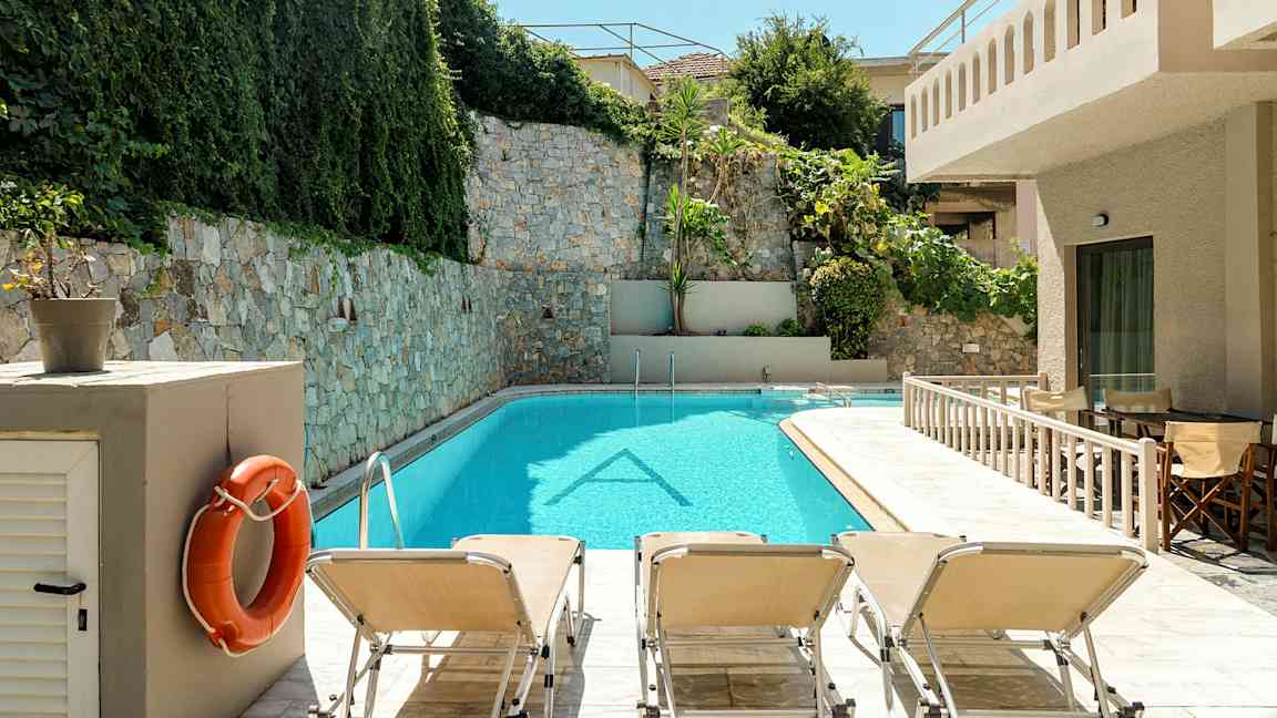 Et basseng omgitt av steinmur og grøntområder. Solsenger står ved bassengkanten. (AI-generert tekst)