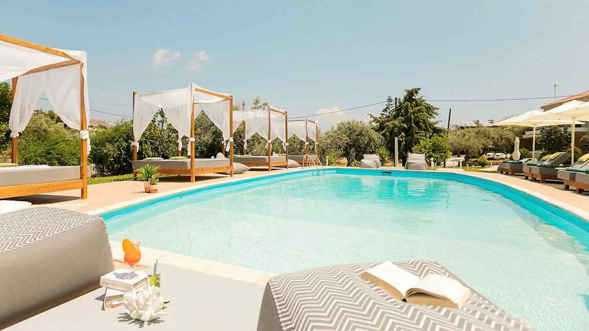 Et svømmebasseng med senger og parasoller rundt. (AI-generert tekst)