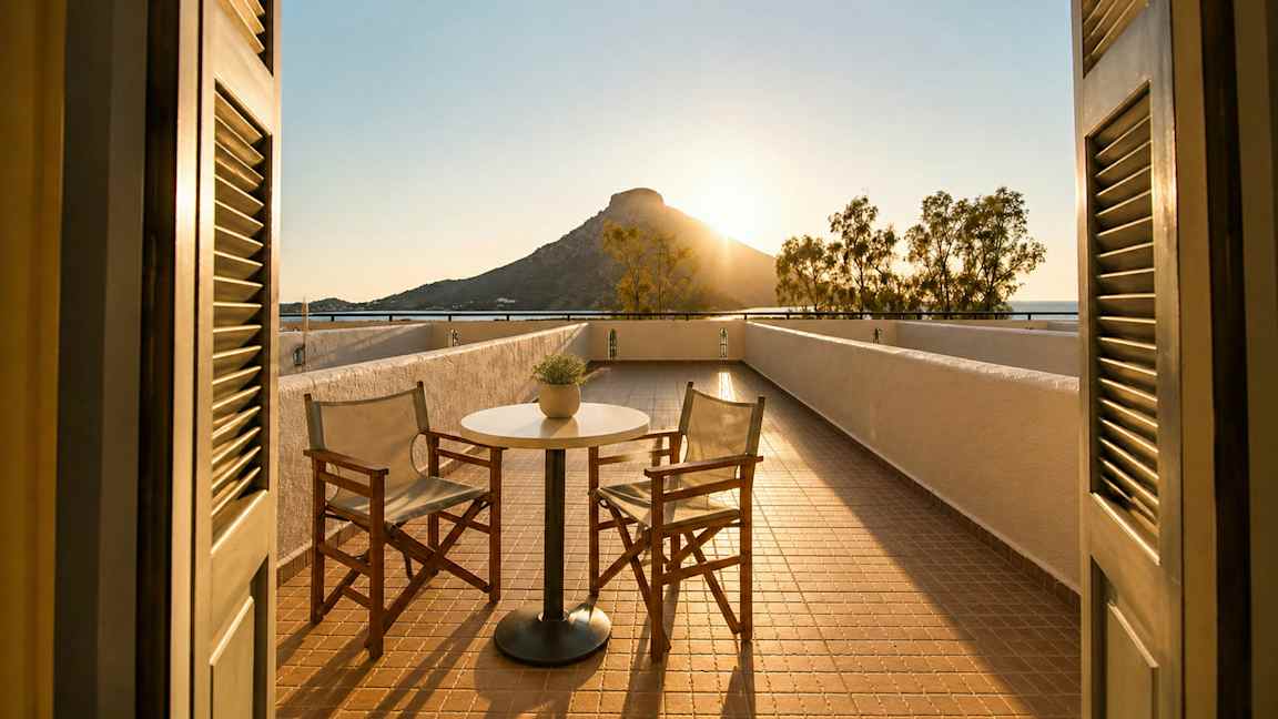En terrasse med to stoler og et bord, med utsikt over et fjell ved solnedgang. (AI-generert tekst)