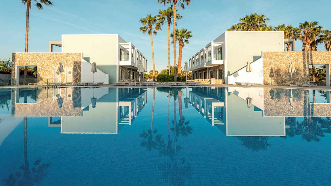 To moderne bygninger ved et basseng med palmer i bakgrunnen. (AI-generert tekst)