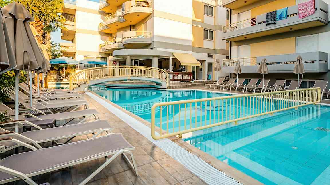 Et utendørs svømmebasseng med solsenger og parasoller ved en moderne bygning. (AI-generert tekst)