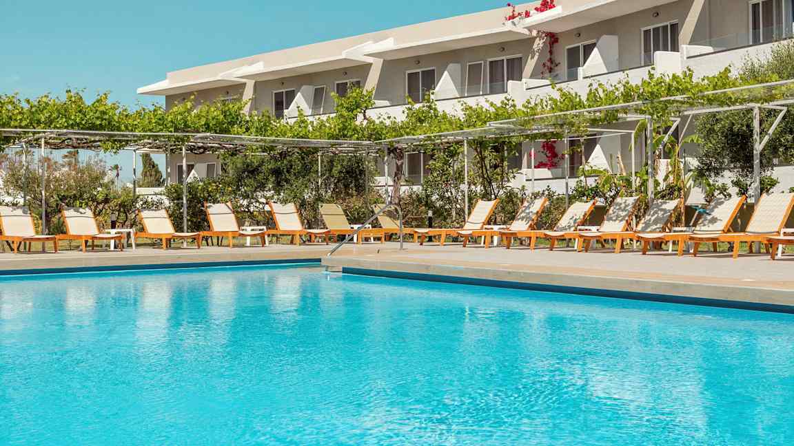 Utendørs basseng foran en rekke solsenger og et hotell i bakgrunnen. (AI-generert tekst)
