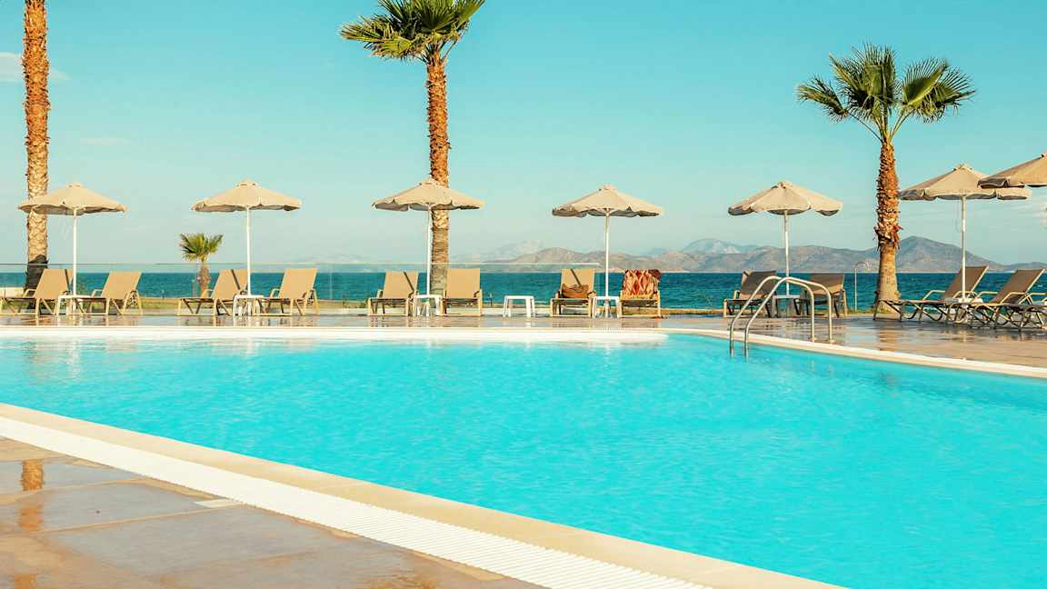 Et basseng med solsenger og parasoller, med havet og fjell i bakgrunnen. (AI-generert tekst)