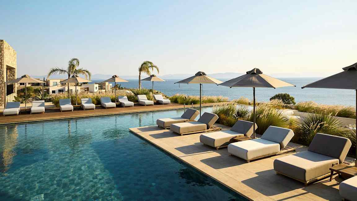 Bassengområde med solsenger og parasoller, utsikt mot havet. (AI-generert tekst)