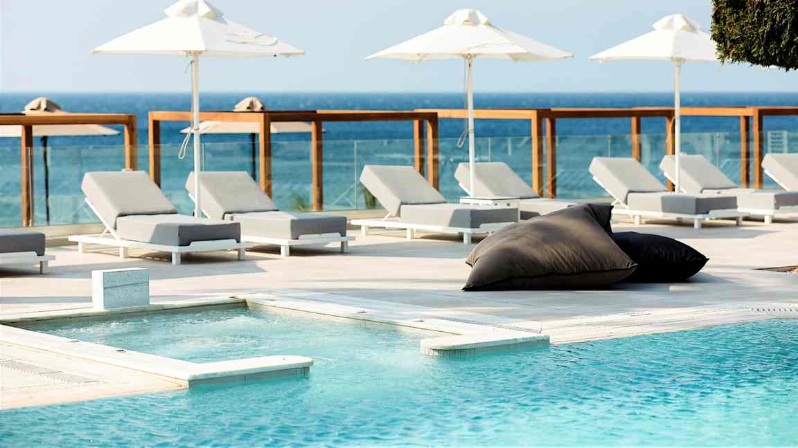 Hvite solsenger og parasoller ved et basseng med havutsikt. (AI-generert tekst)