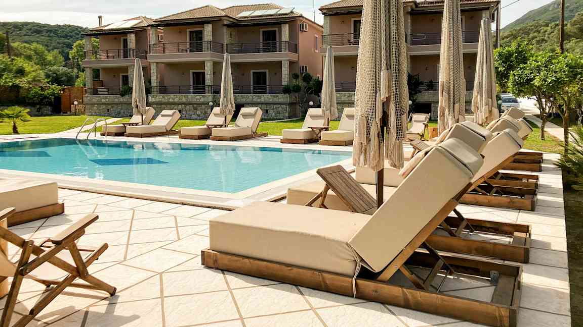 Utendørsbasseng med solsenger og parasoller, omgitt av bygninger og grøntområder. (AI-generert tekst)